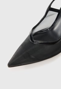 Escarpins noirs à talon aiguille avec un bout pointu, revêtement en maille, texture brillante et intérieur lisse. Présente un design découpé près de la cheville.