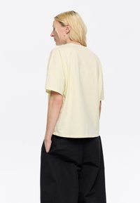 T-shirt in cotone giallo a maniche corte con vestibilità rilassata, dotato di scollatura rotonda e tessuto morbido, abbinato a pantaloni neri larghi.