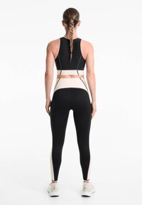 Soutien-gorge de sport noir et leggings ajustés, avec des panneaux latéraux crème et un design épuré. Fabriqué en matériau extensible et respirant.