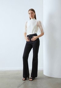 Vit blus med genomskinliga puffärmar, kombinerad med högmidjade svarta utsvängda jeans och svarta klacksandaler. Minimalistisk design och slät textur.