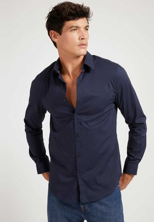 Dark navy long-sleeve shirt made from smooth fabric, featuring a button-up front, collar, and subtle logo detail on the chest.