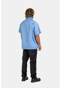 Blue short-sleeve shirt with a straight cut, paired with black corduroy pants. The outfit features a casual design and a relaxed fit.