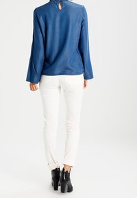 Haut en denim à manches longues de couleur bleu profond avec un détail œillet au dos. Associé à un pantalon blanc à jambes droites et des bottines à talons noires.