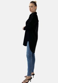 Czarna, oversize koszula z kołnierzykiem na guziki, długimi rękawami i zaokrąglonym dołem, zestawiona z jasnoniebieskimi skinny jeansami i czarnymi, sandałami na wysokim obcasie.