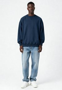 Felpa blu navy con scollo rotondo, maniche raglan lunghe e polsini a coste, abbinata a jeans azzurri e sneakers bianche.