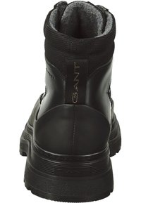 Schwarze Knöchelstiefel mit einer glatten Lederoberfläche, einem strukturierten Stoffkragen und einer gepolsterten Sohle, mit einem dezenten Logo-Detail an der Rückseite.