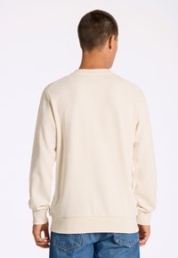 Ljus beige sweatshirt med lång ärm och rundad krage. Har ribbade manschetter och nederkant, tillverkad av mjukt, strukturerat bomullsmaterial.