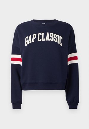 Navy blue cropped collegepaita, valmistettu puuvillasta, jossa on valkoiset "GAP CLASSIC" -tekstit ja punavalkoiset raidalliset yksityiskohdat hihoissa.