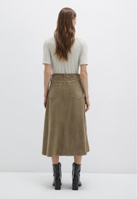Knee-length olive green corduroy skirt featuring a fitted waist, rear pockets, and a slight A-line silhouette, paired with black heeled boots.