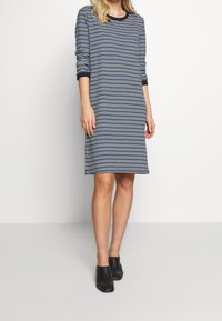 Robe en maille à motif bleu marine et blanc avec manches longues et encolure ronde. Comporte un liseré noir sur l'encolure et les manches.