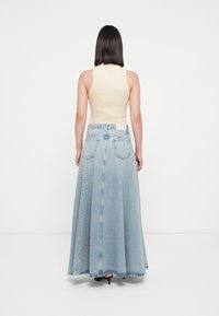 Lys blå denim maxi skjørt med en flytende form, med glidelås bak, to lommer og en teksturert stofffinish. Matchende beige topp.