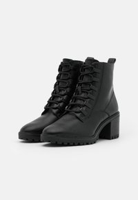 Bottines en cuir noir avec un laçage à l'avant, un talon épais et une semelle texturée. Caractérisées par des coutures renforcées et une languette à l'arrière.