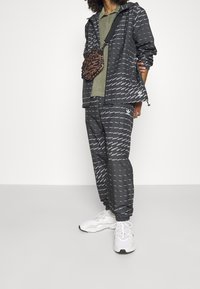 Svart- och vitrandig jacka och byxor i lätt tyg, i kombination med en texturerad brun axelväska och vita sportskor.