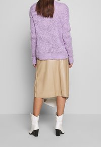 Violetti neulepusero, jossa on väljä istuvuus ja tekstuurinen kuvio, yhdistettynä beigeen nahkahameeseen ja valkoisiin korkokenkiin, jotka ovat cowboy-tyyliset.