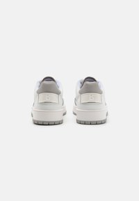 White sneakers with a smooth leather upper, grey accents on the heel, textured tongue, and a rubber sole featuring horizontal grooves.