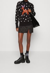 Pull noir à pois blancs et motif de renne marron. Assorti avec une mini-jupe noire à motifs et des bottines noires. Sac fourre-tout noir.