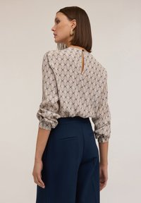 Blusa a maniche lunghe color crema con un motivo geometrico, dotata di scollatura a chiave sul retro e maniche con polsini, abbinata a pantaloni navy a vita alta.