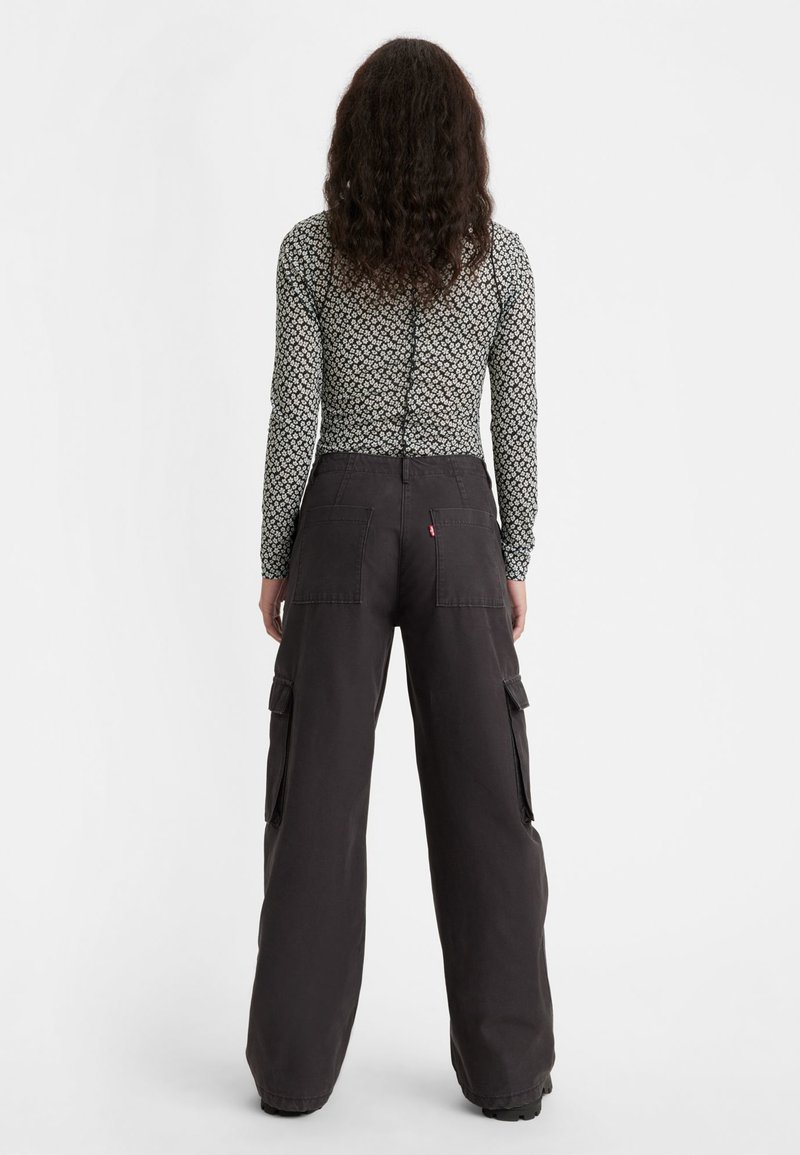 Haut noir à manches longues avec motif floral, associé à un pantalon cargo gris foncé à coupe décontractée, doté de grandes poches latérales et d'une poche arrière.