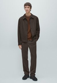 Brun uldblandet jakke med knaplukning, lagdelt over en brun sweater. Matchende brune bukser fuldender outfittet, parret med mørke sneakers.