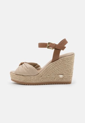 Beige kile-sandal med vævet rebhæl, knyttet frontstofrem og brun justerbar anklerem med gyldent spænde.