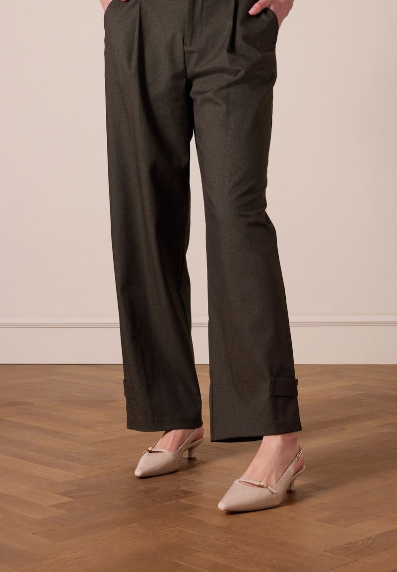 Brede, donkergrijze broeken met voorplooien en enkelboorden, gecombineerd met lichtroze slingback hakken met een spitse neus en een klein metallic detail.