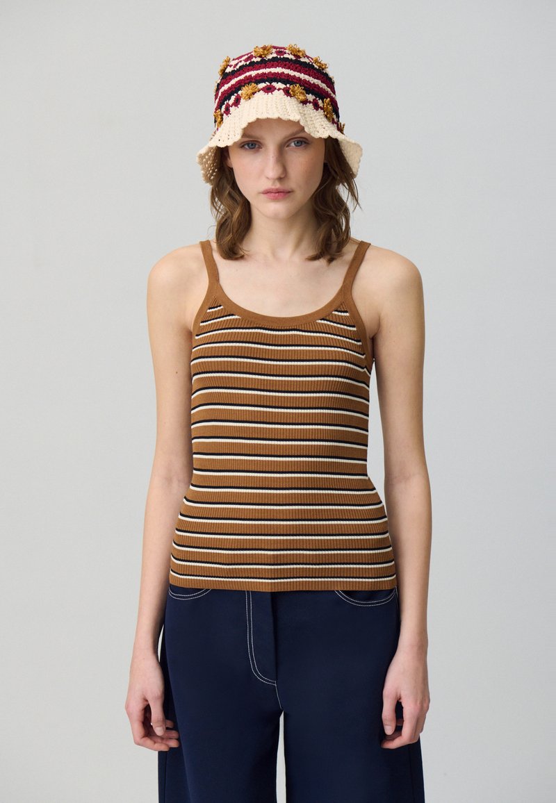 Débardeur marron à côtes avec des rayures horizontales blanches et marron foncé. Association avec un pantalon large bleu marine et un chapeau seau en crochet.