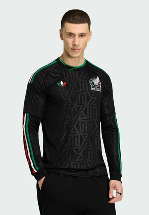 Hombre con camiseta de fútbol de México negra de manga larga con franjas verdes, blancas y rojas en las mangas y logo del equipo de México en el pecho.
