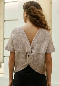 Sweter w miękkim beżu z krótkimi rękawami i głębokim dekoltem z tyłu. Posiada skręconą detalę w okolicy talii oraz luźny krój.