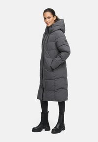 Long grey puffer coat with a hood, featuring quilted design and side pockets; paired with black pants and ankle boots.