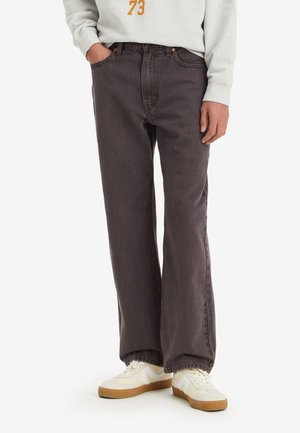 Personne portant un jean large marron foncé avec des baskets blanches et un sweat-shirt gris clair avec le numéro 73 sur la poitrine.