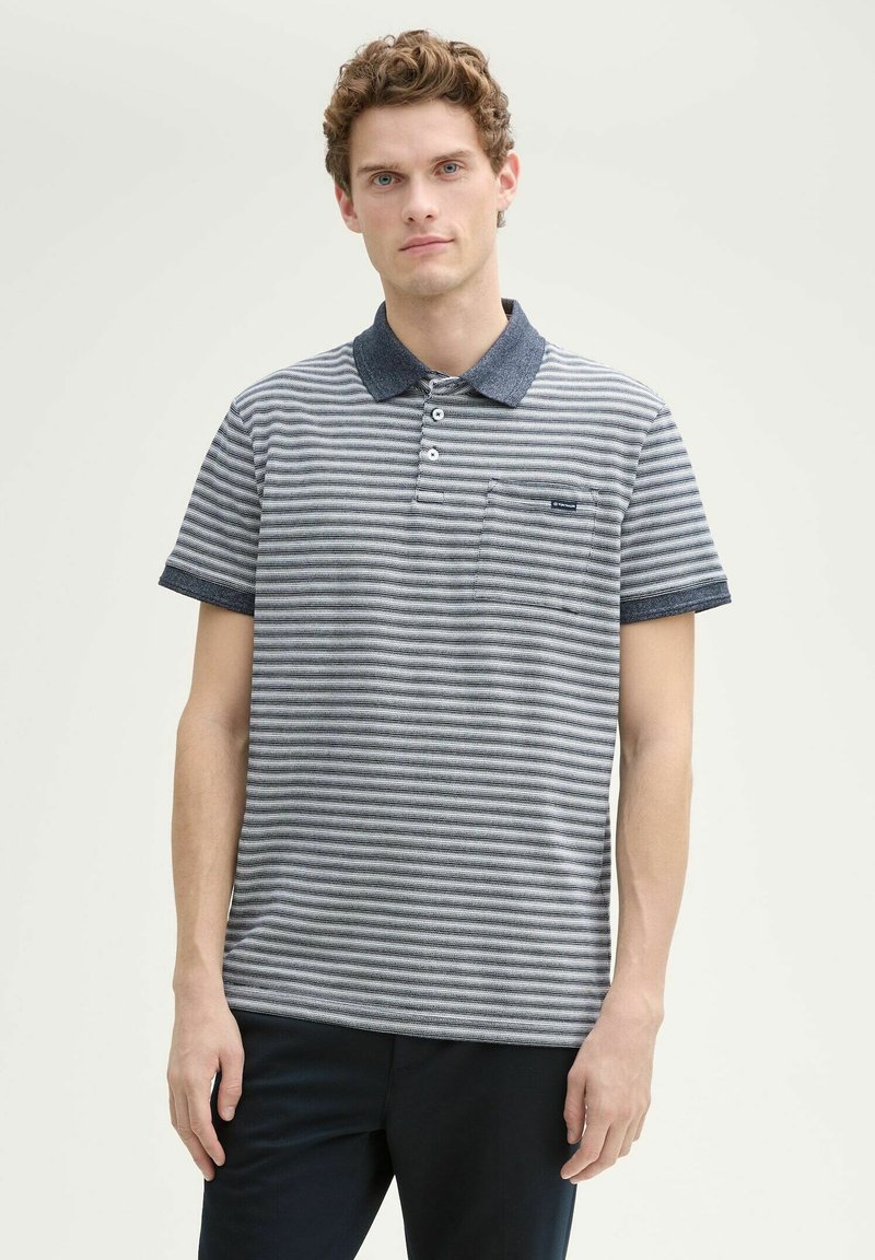 Gestreepte polo in grijs en marineblauw met een effen marineblauwe kraag. Voorzien van een borstzak en korte mouwen, gemaakt van ademende stof.