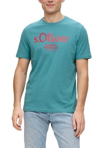Teal katoenen t-shirt met een rood geprint logo, ronde halslijn en korte mouwen, gecombineerd met lichtblauwe denim jeans.