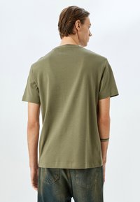 Khaki t-shirt med kortærmer i blødt stof, med rund hals og lige pasform. Synlig syninger og minimal branding på bagsiden.