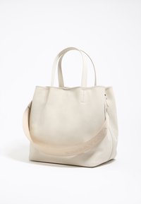 Bolso tote de cuero beige con dos asas y una correa desmontable, que presenta un logotipo en relieve. Textura suave y diseño minimalista.