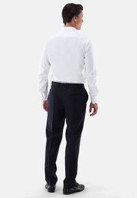 Camicia bianca a maniche lunghe con colletto abbottonato, abbinata a pantaloni eleganti blu navy con tasche posteriori e scarpe eleganti nere.