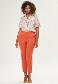 Blusa a maniche corte floreale in azzurro chiaro, rosa e bianco, abbinata a pantaloni arancioni aderenti. Vestibilità slim con una texture liscia e una leggera lucentezza.