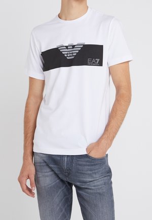 Bílý bavlněný tričko s černým horizontálním panelem, na kterém je šedé logo s křídly a text "EA7". Krátké rukávy a kulatý výstřih.