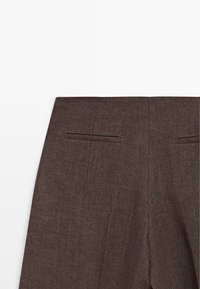 Pantalon marron en mélange de laine avec une ceinture étroite et deux poches passepoilées horizontales à l'arrière sur fond blanc.
