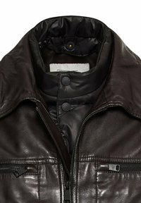 Bruine lederen jas met een hoge kraag, voorzien van een gewatteerde binnenvoering en twee met rits afgesloten voorzakken. Zilveren rits hardware accenten.