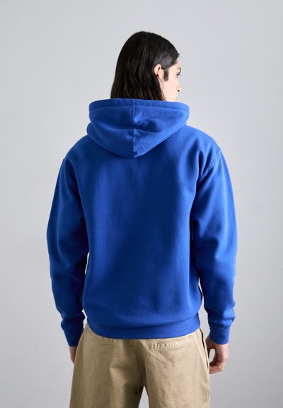 Felpa blu in pile con vestibilità rilassata, polsini e orlo a costine, caratterizzata da un ampio cappuccio. Il tessuto appare morbido con una superficie liscia.