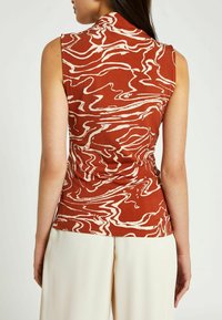 Bezrukávý top v barvě rezavé s abstraktním bílým vlnitým vzorem. Disponuje vysokým límcem a přiléhavým střihem, doplněný krémovými širokými kalhotami.