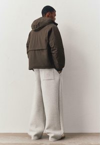 Groene capuchonjas met een losse pasvorm en elastische manchetten, gecombineerd met lichtgrijze sweatpants met brede pijpen en achterzakken.