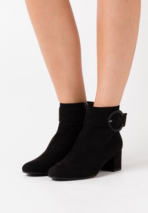 Svarta ankelstövlar i mocka med rundad tå, kort klack och en dekorativ spänndetalj på kanten. Slät textur över hela ytan.