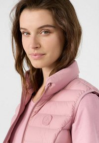 Gilet imbottito rosa chiaro con colletto alto, chiusura a zip e dettaglio con logo. Presenta una texture liscia e motivi di cucitura orizzontale.