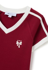 Camiseta roja con escote en V y ribete blanco. Presenta un gráfico de lazo y estrellas en blanco. Fabricada con un tejido suave. Manga corta.