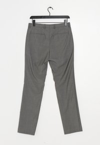 Šedé pánské kalhoty s hladkou tkanou strukturou; úzký střih; poutka na opasek; dvě zadní kapsy; zavěšené na černém plastovém ramínku.
