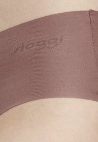 Brauner nahtloser Stoff, der ein glattes Band bildet. Verfügt über einen dezenten Logo-Druck, mit flexibler Textur und minimaler Naht entlang der Kante.