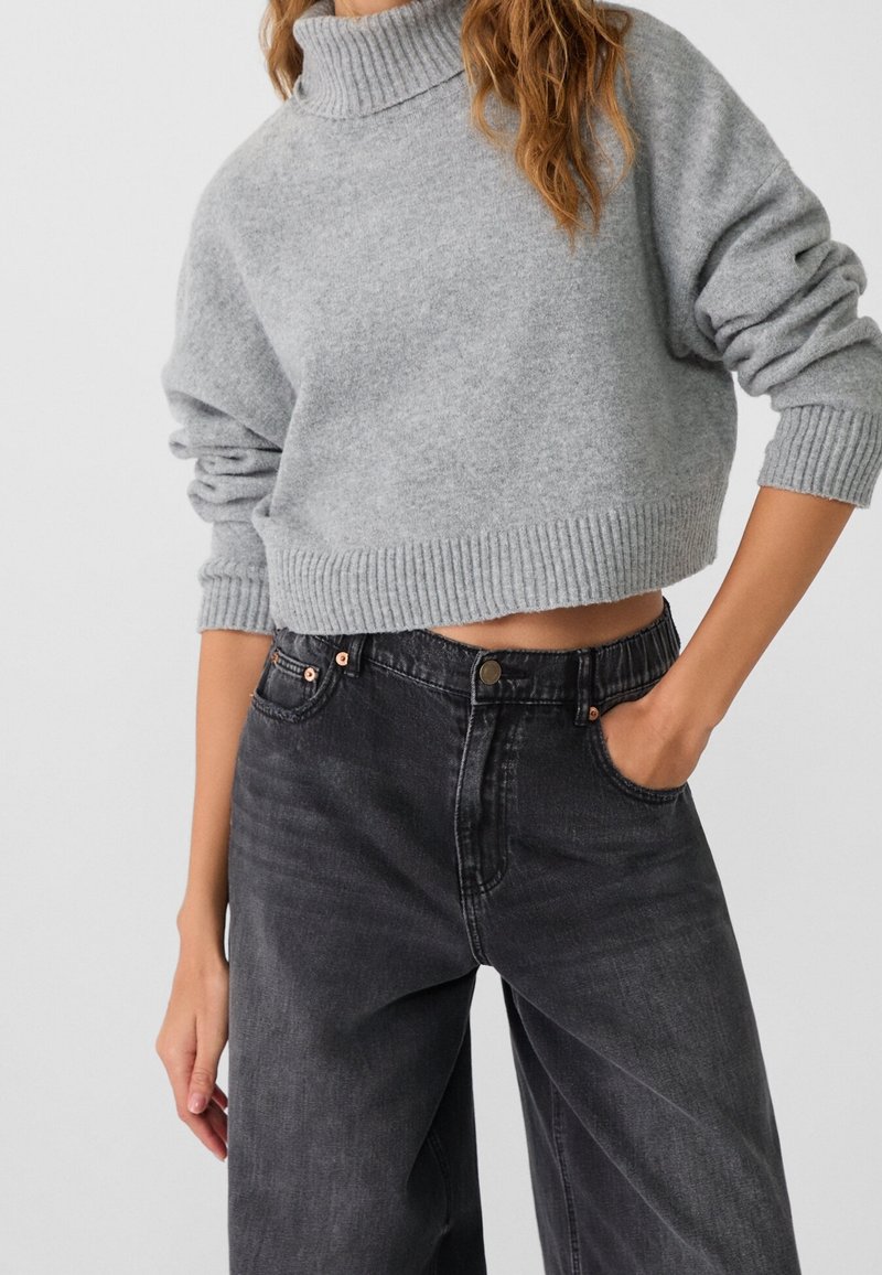 Grijze cropped trui met een hoge hals, met geribbelde manchetten en onderrand, gecombineerd met zwart, hoogzitterwijd kaki jeans.