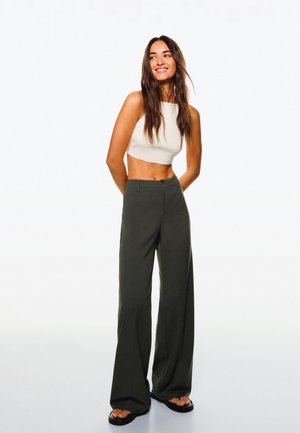 Top alb fără mâneci, decupat, și pantaloni largi cu talie înaltă, verde închis. Material neted, design minimalist și sandale plate.