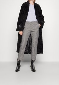 Svart fuskpälsjacka med läderdetaljer vid ärmarna, ljusgrå t-shirt och grå rutiga byxor. Svarta ankelstövlar med dragkedjor fulländar outfiten.